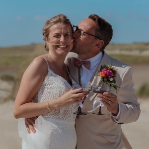 Happy bride and groom celebrating a beach wedding in Denmark with champagne under a blue sky