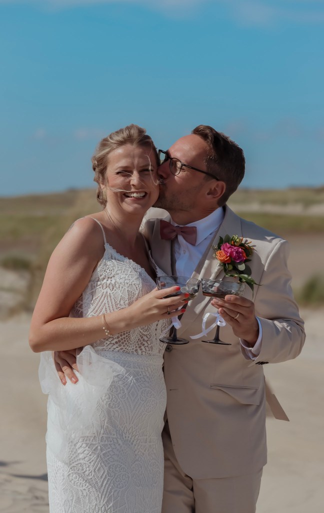 Happy bride and groom celebrating a beach wedding in Denmark with champagne under a blue sky