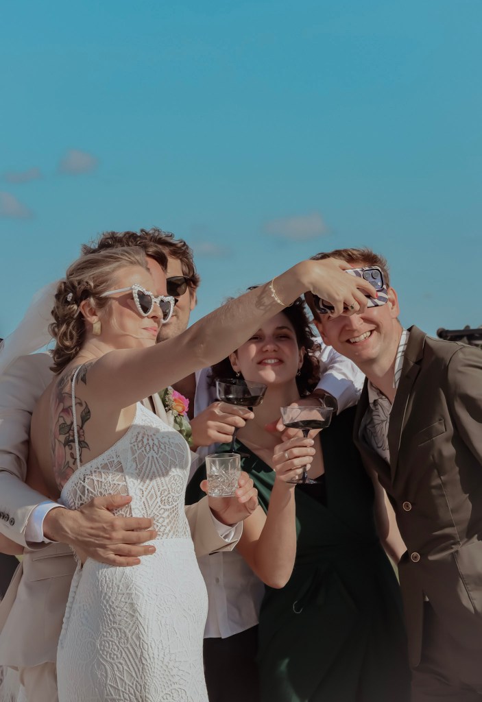 Bride and guests taking a joyful selfie on the beach during a wedding celebration.