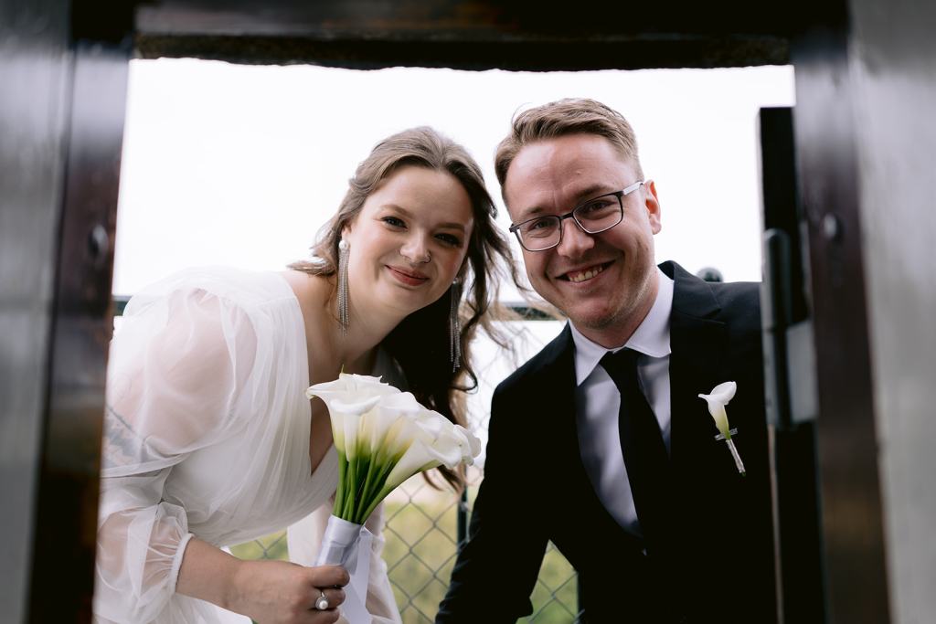 Bride and groom smiling at the camera, the bride holding a bouquet of white calla lilies.