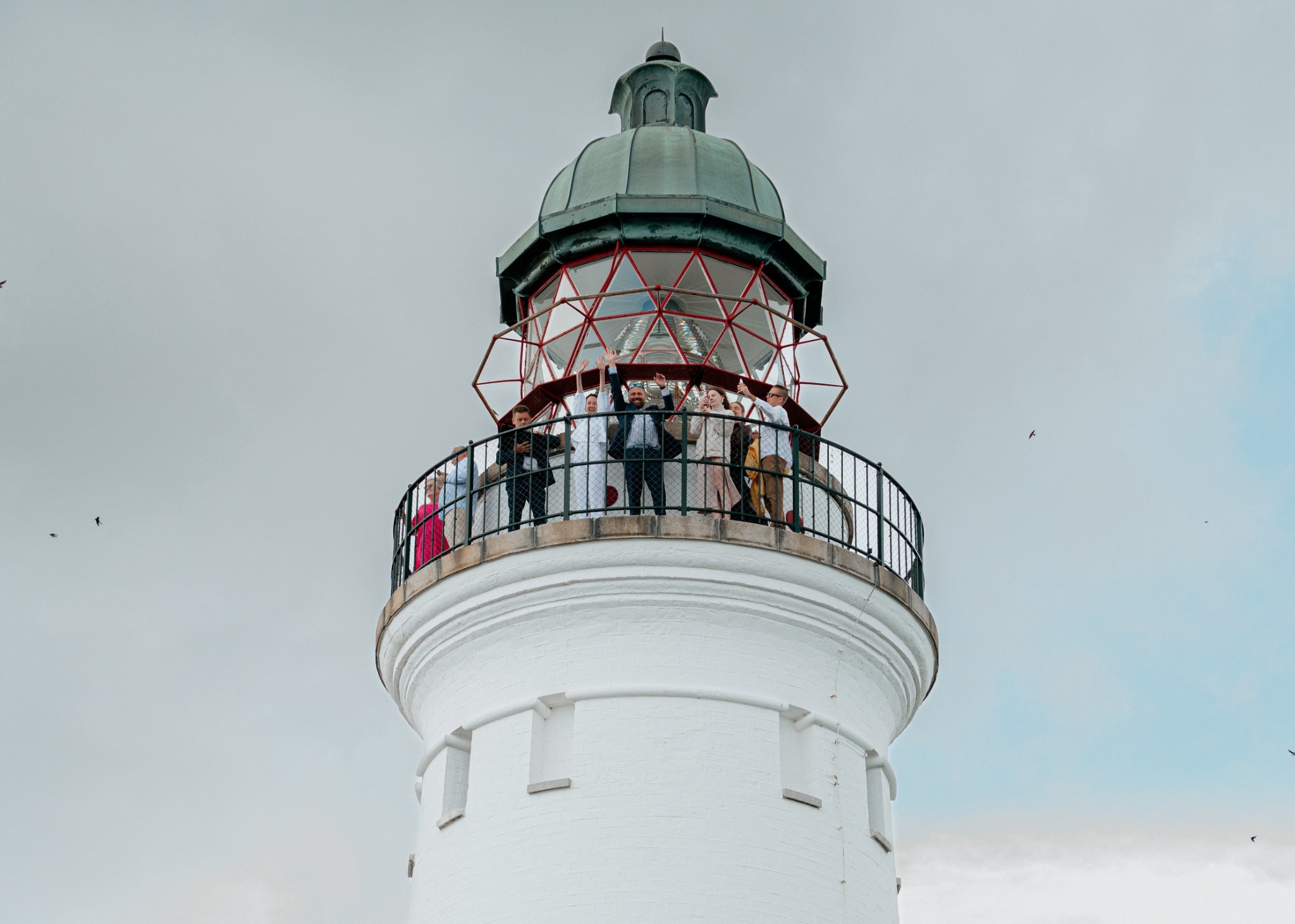 Wedding guests standing on the balcony of a lighthouse, waving and smiling.