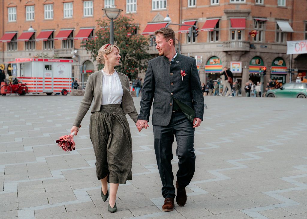 Couple holding hands and walking across a city square after their wedding ceremony, smiling at each other.