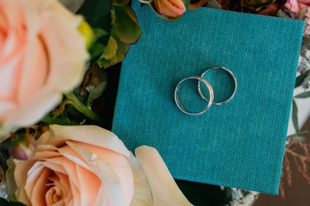 Two wedding rings placed on a teal fabric box surrounded by soft pink roses.