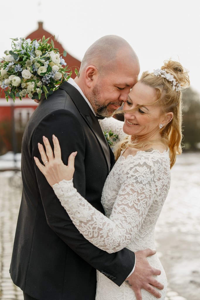 Romantic bride and groom embracing during their wedding in Denmark, with bouquet and historic surroundings in the background.