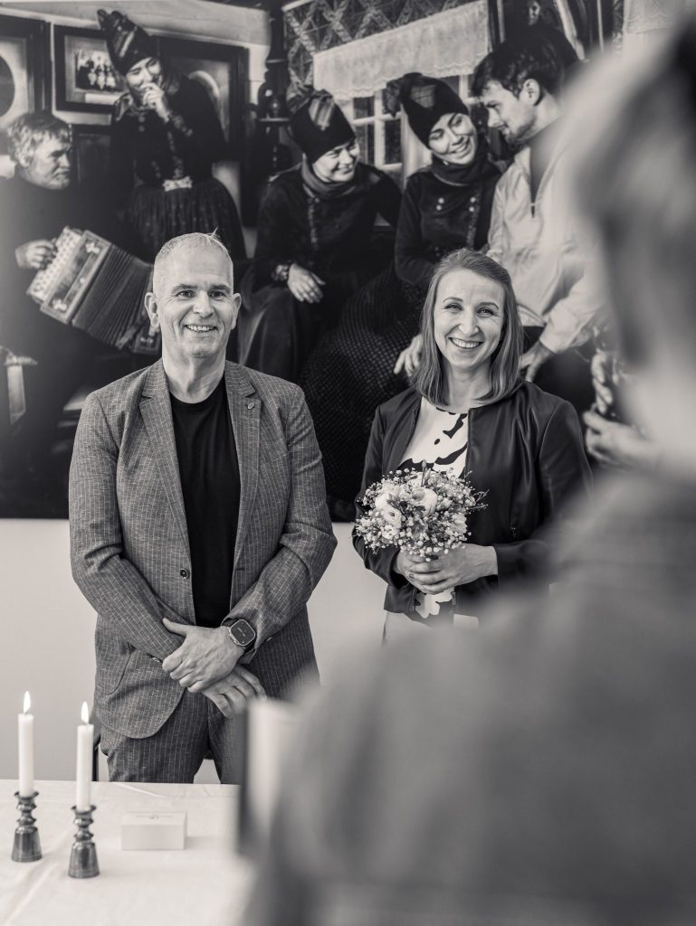 Smiling couple standing during wedding ceremony in black and white.